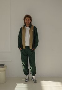 Aktiivne riietus, kus on värviblokiga roheline ja beež jakk, mis on varustatud tõmblukuga, rohelised püksid ja hallid jooksujalanõud. Tekstuuriga kangas.