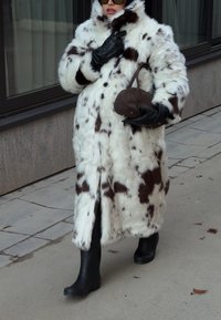 Műszőrméből készült kabát fehér és barna tehénmintával, nagy gallérral, fekete kesztyűvel és egy kis barna kézitáskával. Fekete csizmával viselve.