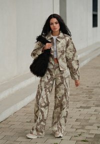 Kamouflage-mönstrad jacka och vida byxor i beige och brunt, kombinerat med en fluffig svart axelväska och vita sneakers.