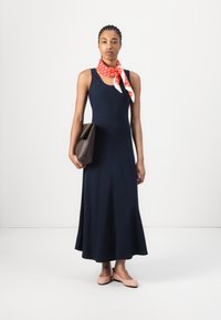 Navy blue sleeveless dress with a flared skirt, paired with a red patterned scarf and a brown handbag. Smooth fabric, minimalistic design.