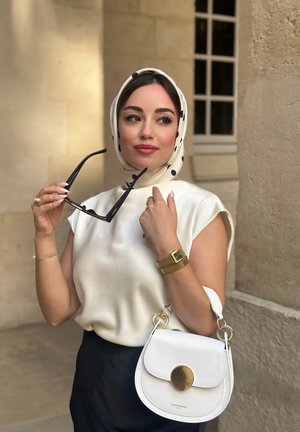 Bolso de cuero blanco con herrajes dorados, blusa de seda de manga corta, falda negra y un pañuelo de lunares. Lleva gafas de sol y usa un reloj dorado.