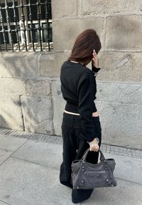 Svart cropped genser med teksturert design, kombinert med løse svarte bukser. Holder en grå lærhåndveske med nagledetaljer.