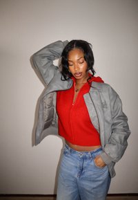 Veste matelassée grise avec un col structuré, portée sur un pull court en tricot rouge, associée à un jean taille haute bleu clair.