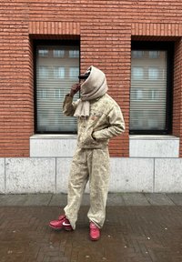 Μπεζ τζιν μπουφάν με μοτίβο και ταιριαστά παντελόνια με άνετη γραμμή, συνδυασμένα με κόκκινα αθλητικά παπούτσια Nike και ένα ελαφρύ κασκόλ που καλύπτει το πρόσωπο.