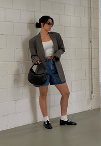 Γκρι καρό oversized σακάκι, λευκό crop top, τζιν σορτς, μαύρη πλεκτή τσάντα και γυαλιστερά μαύρα slip-on παπούτσια με λευκές κάλτσες.