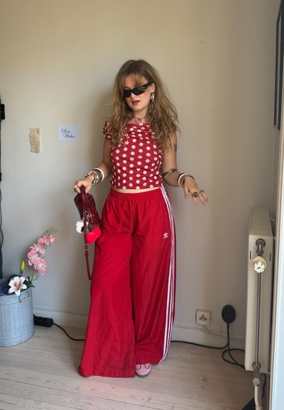 Top corto rojo con lunares y volantes en los hombros, combinado con pantalones rojos holgados con rayas blancas. Los accesorios incluyen pulseras en capas y un bolso rojo.