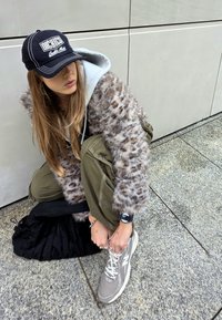 Tehispehmed karvapestud leopardimustriga, hall kapuutsiga särk all, oliivrohelised cargo-püksid, must müts ja hallid New Balance spordijalatsid.