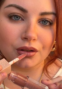 Maybelline Lipgloss in einer klaren Tube mit einem beigefarbenen Etikett; verfügt über einen weichen Applikator; der Gloss wirkt auf den Lippen nackt.