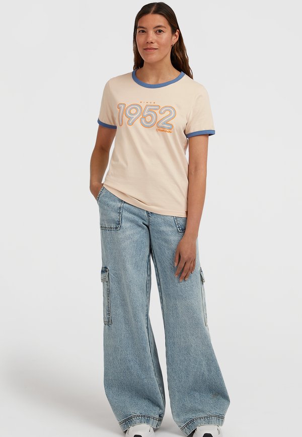 Ljusbeige t-shirt med blå krage och ärmar, med fet orange text "1952" och en avslappnad passform. Kombinerad med vida denimbyxor.