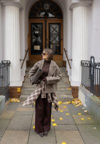 Koszula w kratę, brązowy golf i szerokie bordowe spodnie. Dodatki to ciemna torebka i okulary przeciwsłoneczne. Schody ozdobione żółtymi liśćmi.