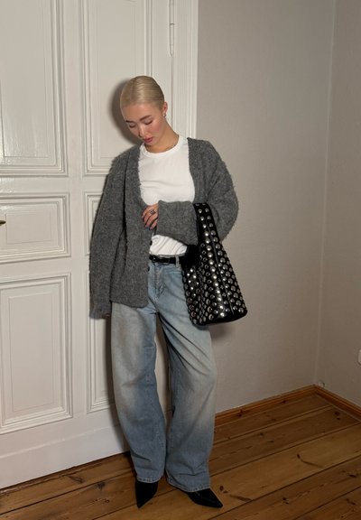 Un cárdigan gris de textura suave sobre una camiseta blanca, combinado con unos vaqueros de pierna ancha de color azul claro. Un bolso negro con tachuelas metálicas completa el conjunto.