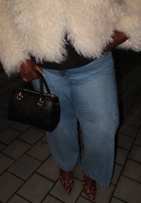 Άτομο που φοράει ανοιχτό μπλε τζιν με φαρδιά πόδια, μυτερές γόβες με λεοπάρ σχέδιο, μια αφράτη λευκή ζακέτα και κρατάει μια μαύρη τσάντα χειρός.