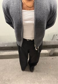 Szürke cipzáras kardigán texturált mintával, fehér bordázott ujjatlan felsővel, laza fekete nadrággal és fekete cipővel párosítva. Kulcstartó látható.