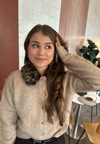 Cardigan beige con bottoni e colletto in pelliccia sintetica a stampa leopardata; motivo a maglia lavorata e polsini a coste. Capelli lunghi e ondulati e orecchini visibili.