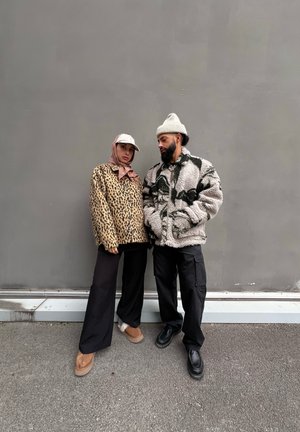 Chaqueta de forro polar de leopardo y chaqueta de forro polar gris con patrón; ambas son de corte oversized, combinadas con pantalones negros y calzado en colores contrastantes.