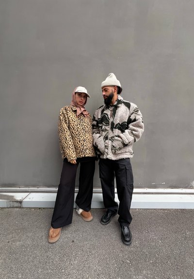 Chaqueta de forro polar de leopardo y chaqueta de forro polar gris con patrón; ambas son de corte oversized, combinadas con pantalones negros y calzado en colores contrastantes.