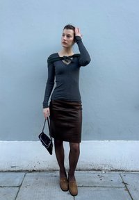 Haut gris à manches longues côtelé avec un col en V et un détail noué, associé à une jupe crayon en cuir marron. Accessoires comprenant un sac à main noir et des mocassins.
