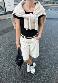 Λευκά σορτς, μαύρη μπλούζα, μπεζ ζακέτα ριγμένη στους ώμους, μαύρη τσάντα, λευκά αθλητικά. Υφασμάτινη υφή και ζώνη με σχέδιο.