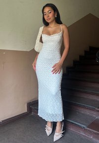 Hvit blonde maksi-kjole med spagettistropper, figursydd silhuett og teksturert mønster. Kombinert med beige spisse hæler og en heklet veske.