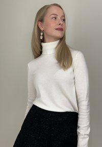 Balts augsts apkakles džemperis ar garām piedurknēm, izgatavots no mīksta auduma. Kombinēts ar melnu teksturētu svārku, kam ir nedaudz spīdīga virsma.