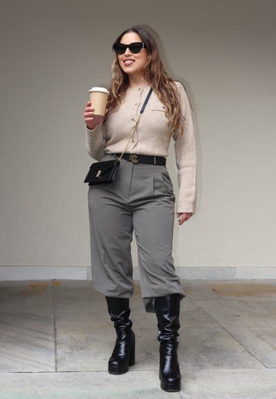 Cardigan de lana beige con botones, pantalones de cintura alta grises, cinturón negro de hebilla, bolso de hombro negro y botas altas con tacón negras.