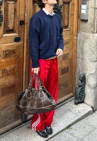 Velika rjava usnjena torba z belim šivom, kombinirana z mornarsko modrim puloverjem, sivo majico in rdečimi satenskimi hlačami s stranskimi črtami.