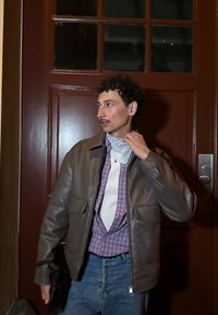 Brun läderjacka med två framfickor, en vit halsduk och en lila rutig skjorta, kombinerad med ljusblå jeans och en svart väska.