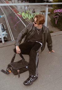 Svart skinnjakke over en mørk genser, kombinert med svarte jeans med hvite striper. Tilbehøret inkluderer lagdelte sølvkjeder og en svart veske.