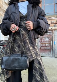 Sort bomberjakke med pelsforet hætte, lagdelt over en beige ternet slip kjole. Sort håndtaske med rektangulær form og sølvfarvet beslag.