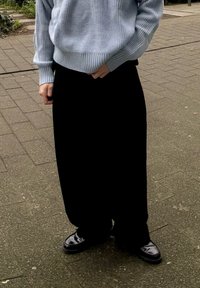 Ανοιχτό μπλε, υφασμάτινο πλεκτό πουλόβερ και χαλαρές μαύρες παντελόνες, συνδυασμένα με μαύρα γυαλιστερά παπούτσια σε κυβικό εξωτερικό χώρο.