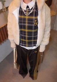 Άτομο που φοράει λευκό γούνινο μπουφάν, μαύρο και κίτρινο πουροφό πουλόβερ με μαργαριτάρια, μαύρο παντελόνι φόρμας Adidas και κρατώντας μια χρυσή τσάντα.