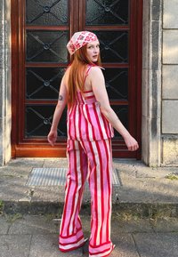 Rožu un sarkanu svītru auduma komplekts ar brīvi pieguļošu augšu un plašām biksēm. Izmēru pielāgojoša rozā šalle papildina izskatu.