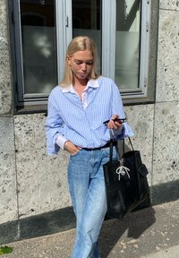 Ανοιχτό μπλε και λευκή ριγέ πουκάμισο με κουμπιά, συνδυασμένο με ανοιχτό τζην. Κρατά μια μαύρη τσάντα tote που διαθέτει ένα γούστο. Απαλές υφές.