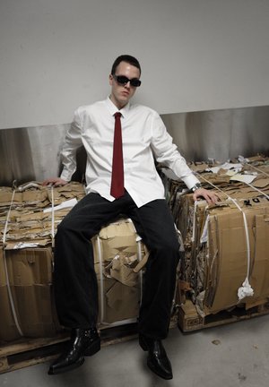 Chemise blanche à boutons, cravate rouge, jeans foncés, lunettes de soleil noires et bottes à talons noires sur un fond en ballot de carton avec une texture froncée.