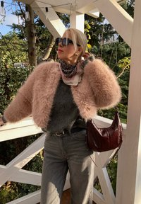 Ροζ πλουμιστή κοντή ζακέτα πάνω από ένα γκρίζο πουλόβερ, σε συνδυασμό με γκρίζα τζιν ψηλής μέσης. Ένα δερμάτινο μπορντό τσαντάκι και ένα κασκόλ με σχέδιο ολοκληρώνουν την εμφάνιση.