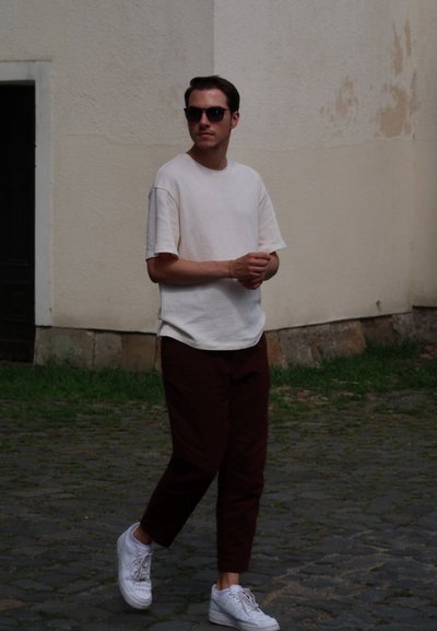 Conjunto informal que incluye una camisa de manga corta de tejido ligero, pantalones burdeos y zapatillas blancas; usando gafas de sol oscuras. De pie al aire libre.