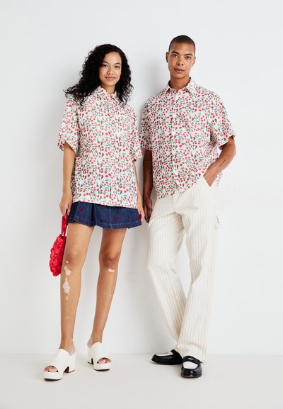 Camisas de manga corta con estampado floral en rosa y verde, combinadas con una falda de mezclilla y pantalones a rayas. Zapatos de tacón blanco y calzado negro.