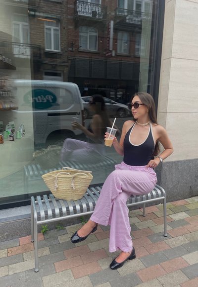 Monosuit de rayas en blanco y negro, pantalones de pierna ancha de rayas rosa claro, bolso de mimbre y bailarinas negras sobre un banco de metal.