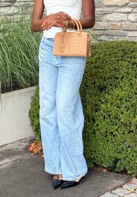 Handtas van tankleurig krokodillenleer met dubbele handvatten. Lichtblauwe wijde spijkerbroek van denim met een rafelige zoom. Zwarte schoenen met een puntige neus.