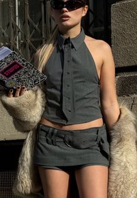 Pilkas halterio viršus su mygtukų detalėmis derinamas su atitinkančia mini sijoną, turinčiu diržą ir kišenę. Modelis laiko raštuotą užrašų knygelę.
