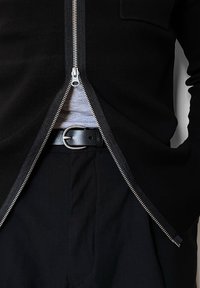 Μαύρο πλεκτό πουλόβερ με φερμουάρ μπροστά, αποκαλύπτοντας μια γκρι μπλούζα από κάτω. Μαύρη ζώνη με μεταλλικό κούμπωμα που ταιριάζει με μαύρο παντελόνι.