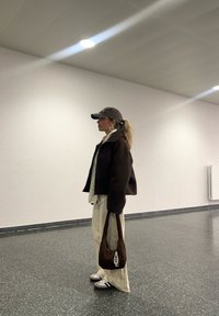 Brun kort jacka över vit skjorta, beige vida byxor, grå keps, hoops örhängen, brun vadderad handväska och bruna sneakers med vita detaljer.