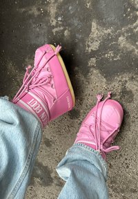 Roze boots met een glanzende afwerking, voorzien van een hoge bovenkant, unieke veters en een lichte zool. Draag ze met ruime, lichtgekleurde denim jeans.