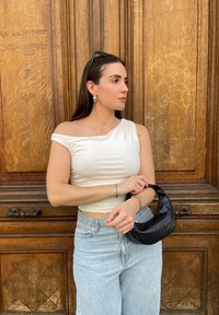 Λευκή τοπ με ένα ώμο, ανοιχτό μπλε παντελόνι με φαρδιά πόδια, μαύρη υφασματοποιημένη τσάντα. Απλά κοσμήματα, σε ξύλινο φόντο.