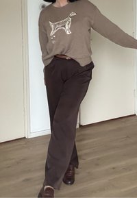Pull marron tricoté avec un motif de chien, associé à un pantalon marron foncé. La tenue comprend une ceinture marron assortie et des chaussures marron.