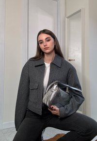 Γκρίζο μάλλινο σακάκι με γιακά, δύο μπροστινές τσέπες και ασημένια μεταλλική τσάντα χειρός. Μαύρα τζην ολοκληρώνουν το σύνολο.