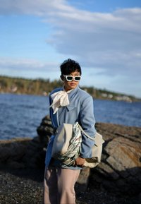 Hele sinine kohandatud jakk, valge sall ja beežid püksid. Hoides beeži kotti, millel on mustriline rihm. Valged päikeseprillid täiustavad välimust.