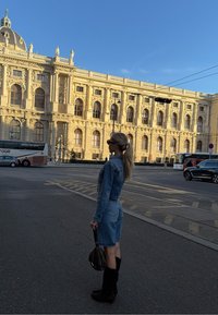 Traper haljina s pripijenim strukom i krojem do koljena, uparena s crnim čizmama do koljena. Dodaci uključuju smeđu, okruglu torbu.