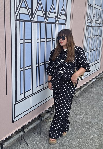 Conjunto de lunares en blanco y negro que incluye una blusa con mangas abullonadas y pantalones de pierna ancha, combinados con gafas de sol negras y un bolso estampado.