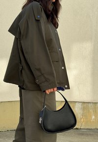 Σκούρο πράσινο oversize σακάκι με κουμπιά σνάπ και πλαϊνές τσέπες, σε συνδυασμό με ταιριαστά παντελόνια. Μικρή μαύρη δερμάτινη τσάντα με καμπυλωτή σχεδίαση.